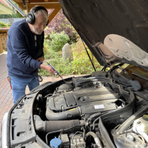 Ein Bediener misst mit einem elektronsichen Stethoskop im Motorraum eines KFZ